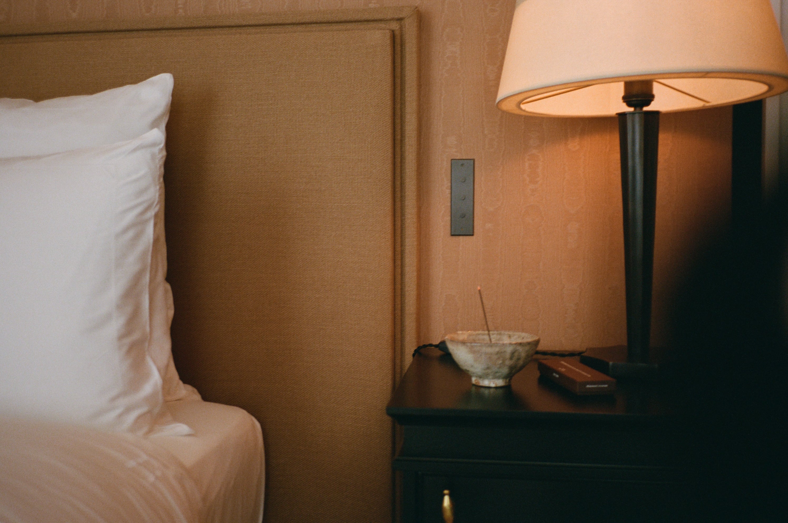 Japanese Incense sticks burning in an incense holder next to a bed and a lamp in a luxury hotel.
